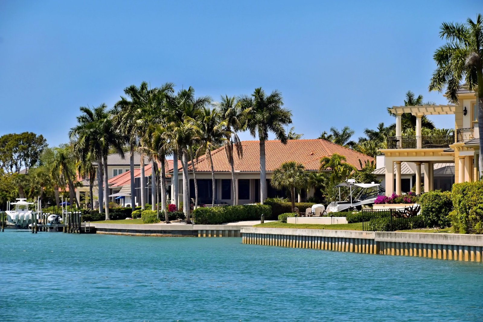 Waterfront homes lined with royal palms along a calm Florida intracoastal channel, with boats moored at private docks